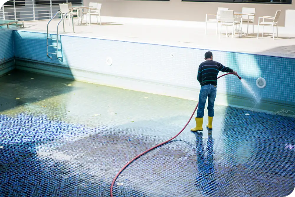 Man cleaning empty swimming pool with hose