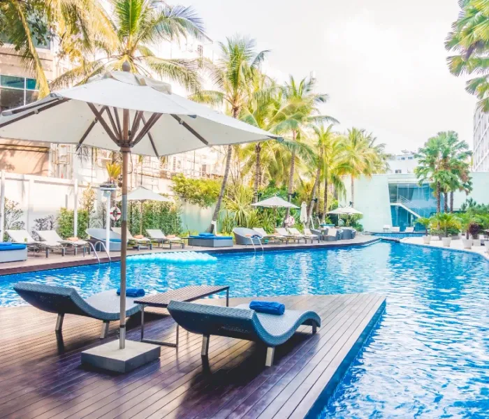Outdoor pool with palm trees, umbrellas, and lounge chairs