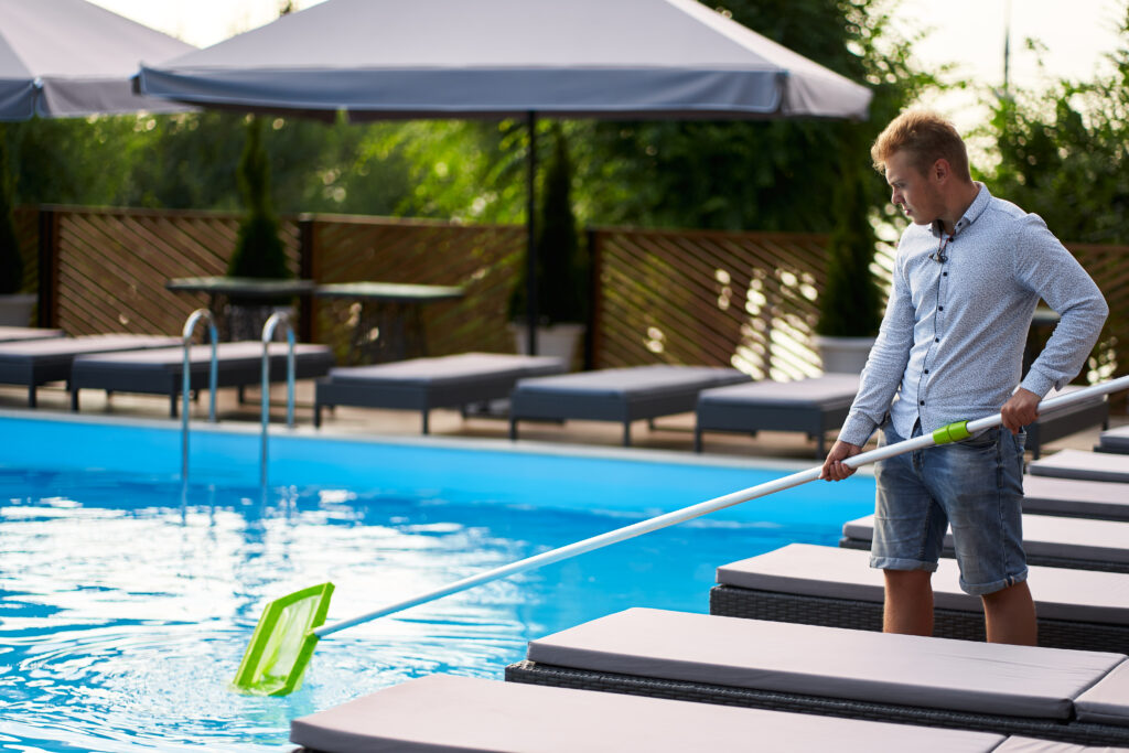 Victoria, TX Experts in Commercial Pool Management Near Me 2 man with skimmer net equipment cleaning swimming pool from rubbish service maintenance pool male removes garbage from water with sap swimming pool cleaning service hotel cleaner